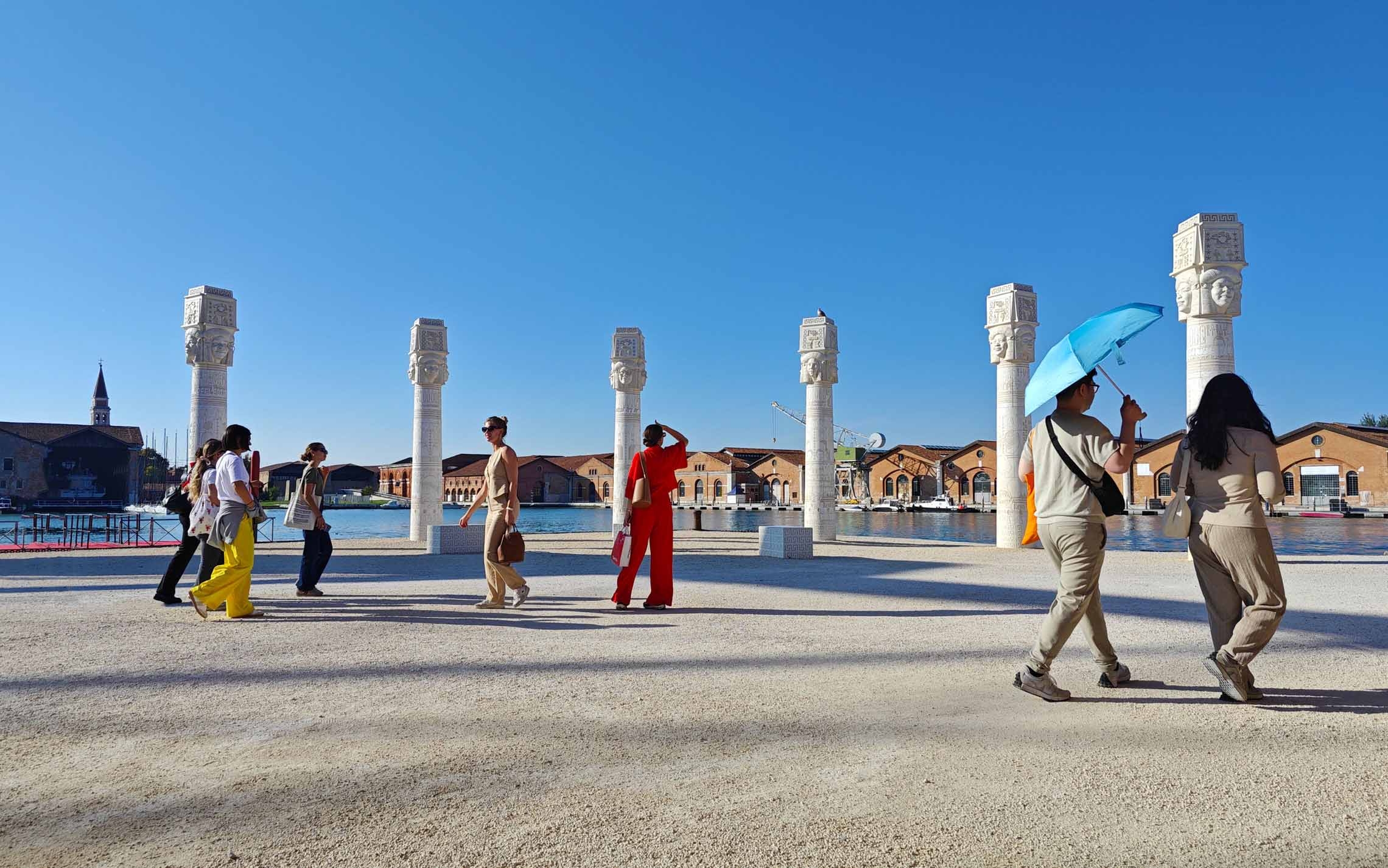 People walking at the Arsenale in front of Lauren Halsey's work titled Keepers of the Krown (2024) exhibited for the first time at the Venice Biennale. People walking at the Arsenale in front of Lauren Halsey's work titled Keepers of the Krown (2024) exhibited for the first time at the Venice Biennale.